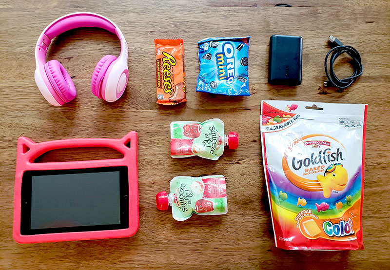 TSA quick bag contents for traveling with kids: headphones, snacks, a tablet, and a portable charger.