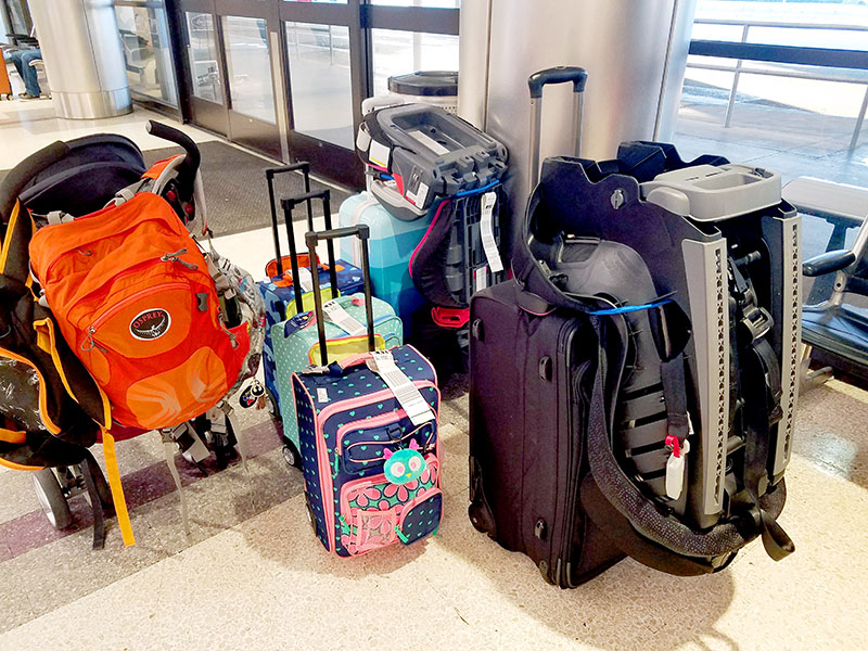 A family's mass of suitcases and car seats in the airport lobby.