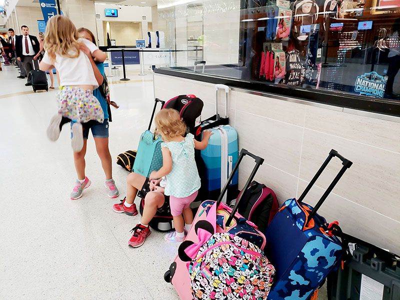 Children waiting with suitcases near airport security.